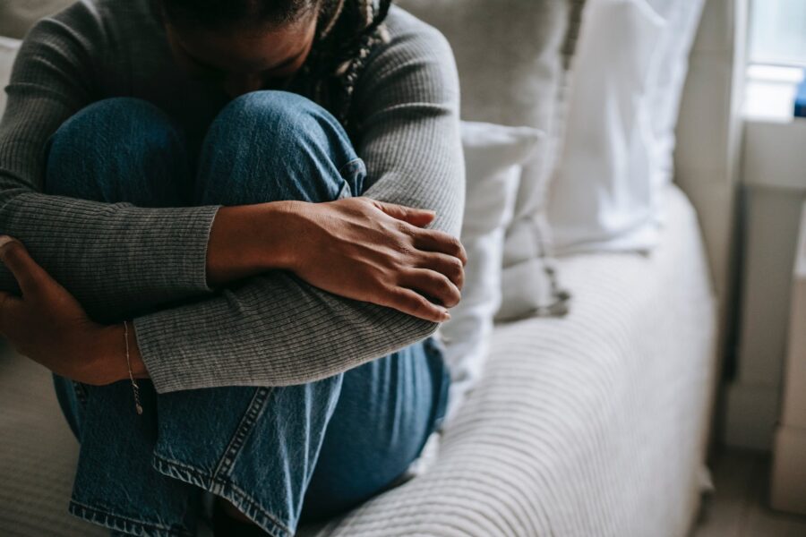 crop pitiful black woman embracing knees on bed